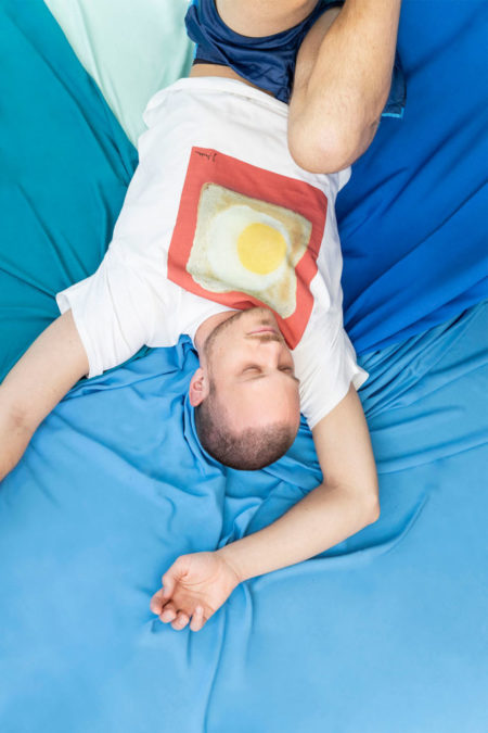 Eine Person liegt auf dem Boden und trägt ein T-Shirt mit einem Spiegelei in Toast drauf.